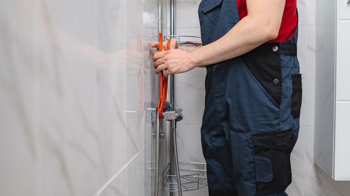 Plumber using pliers to fit a shower mixer in a tiled bathroom