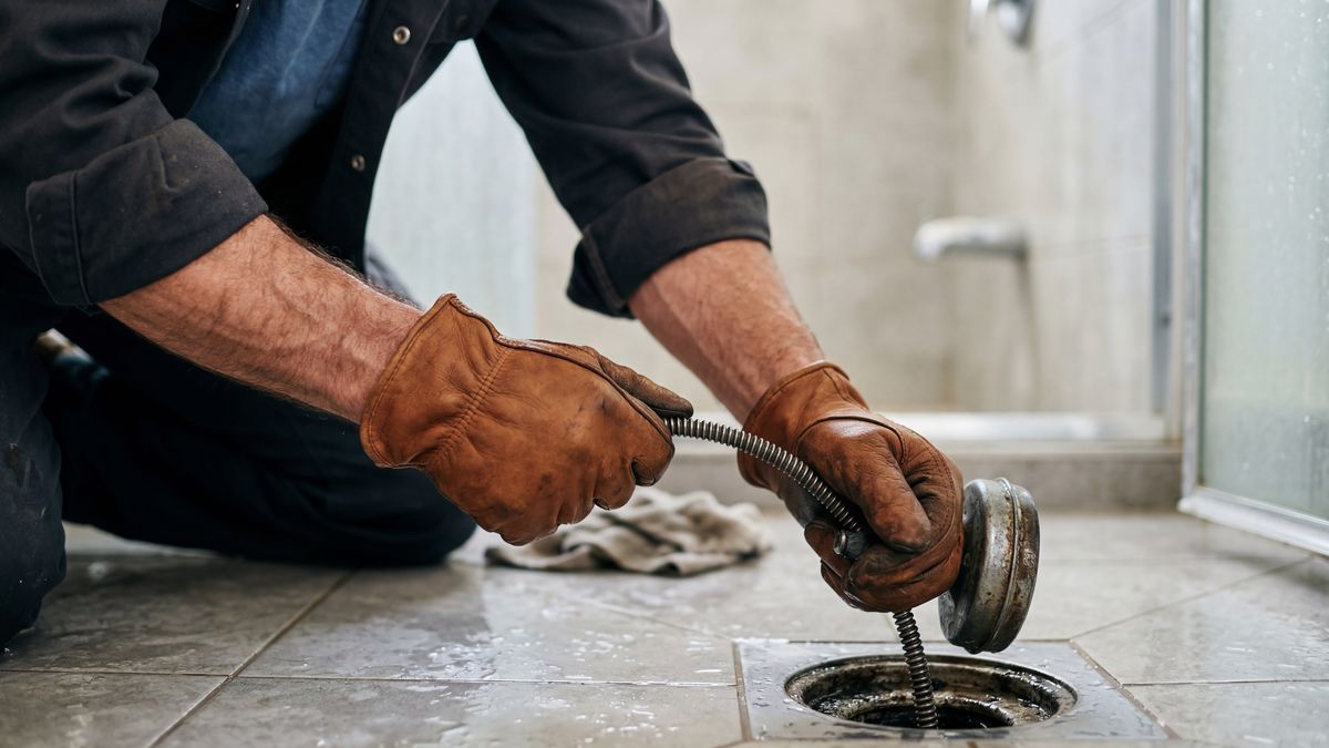 Gloved hands of a plumber lifting the strainer and clearing a shower drain